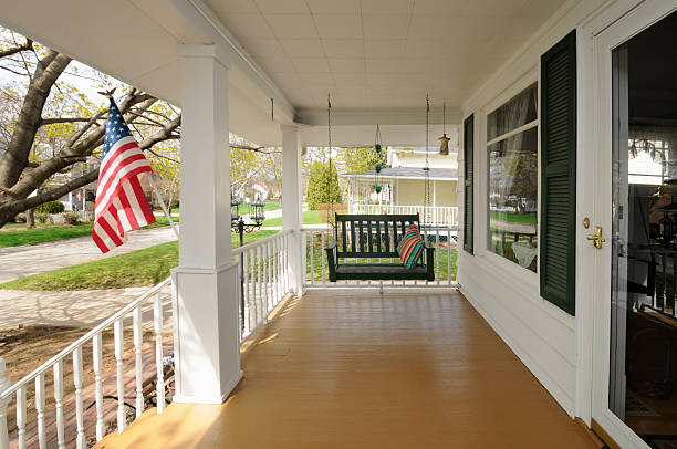 This is a traditional wooden front porch with swinging seat and white pillars. An American flag is displayed in the front yard.